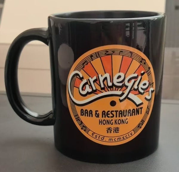 A black ceramic mug printed with a round orange-and-white bar and restaurant logo.